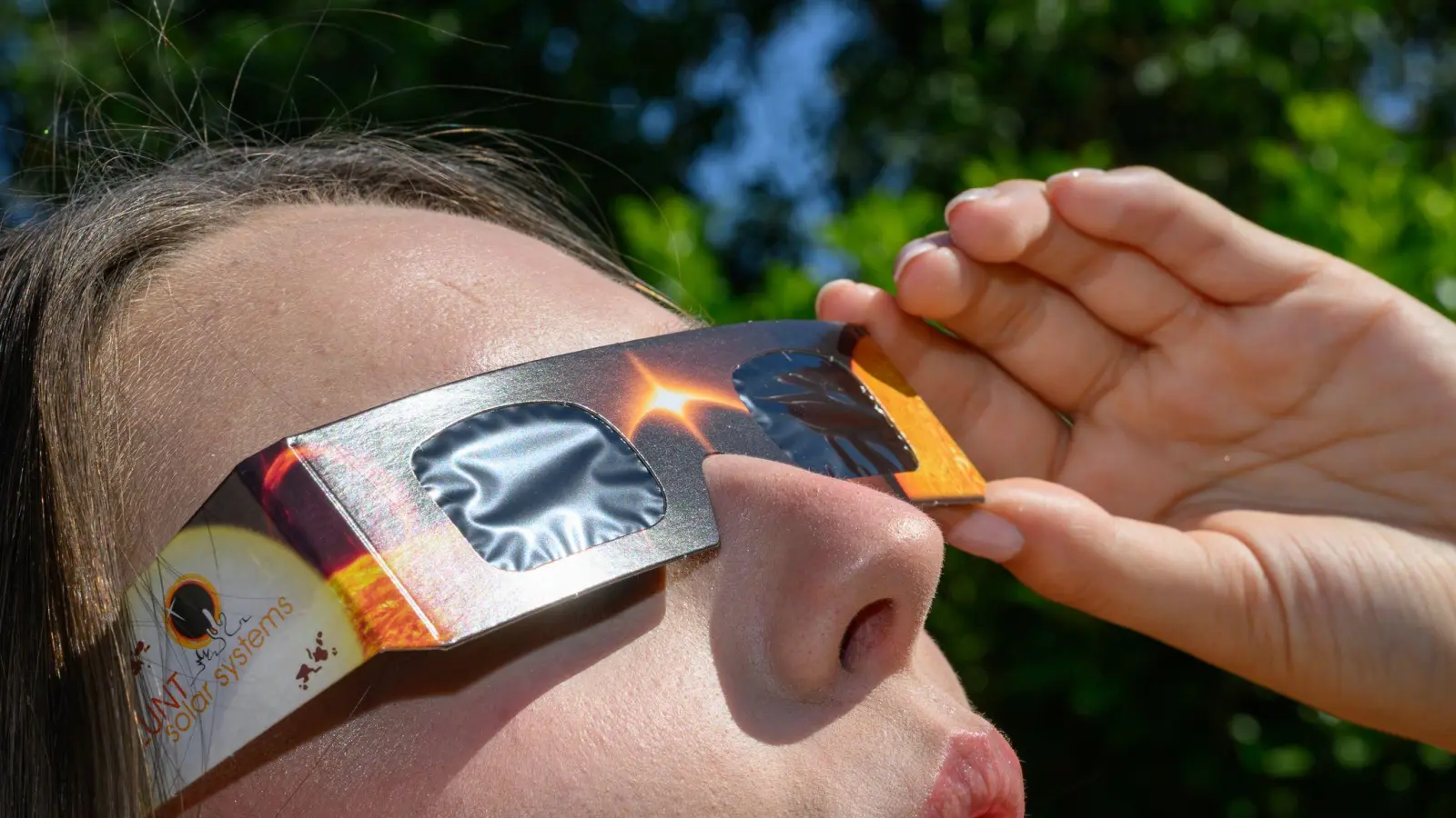 Eine junge Frau schaut durch eine Sonnenfinsternisbrille und betrachtet die Mittagssonne. (Bild: Patrick Pleul/dpa)