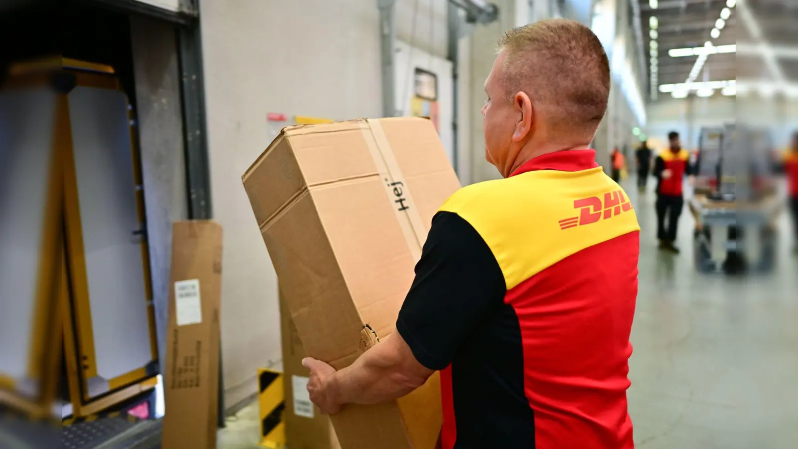 Ein Paketbote schleppt in einem DHL-Standort ein schweres Paket. (Archivbild) (Bild: Sebastian Christoph Gollnow/dpa)
