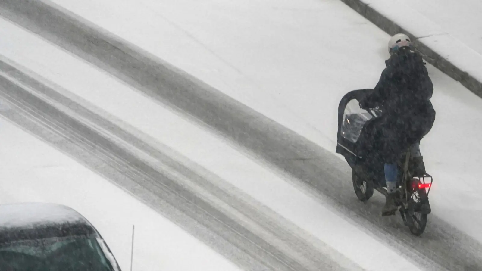 Eine Frau fährt mit einem Lastenfahrrad in Hamburg über eine verschneite Straße. (Bild: Marcus Brandt/dpa)