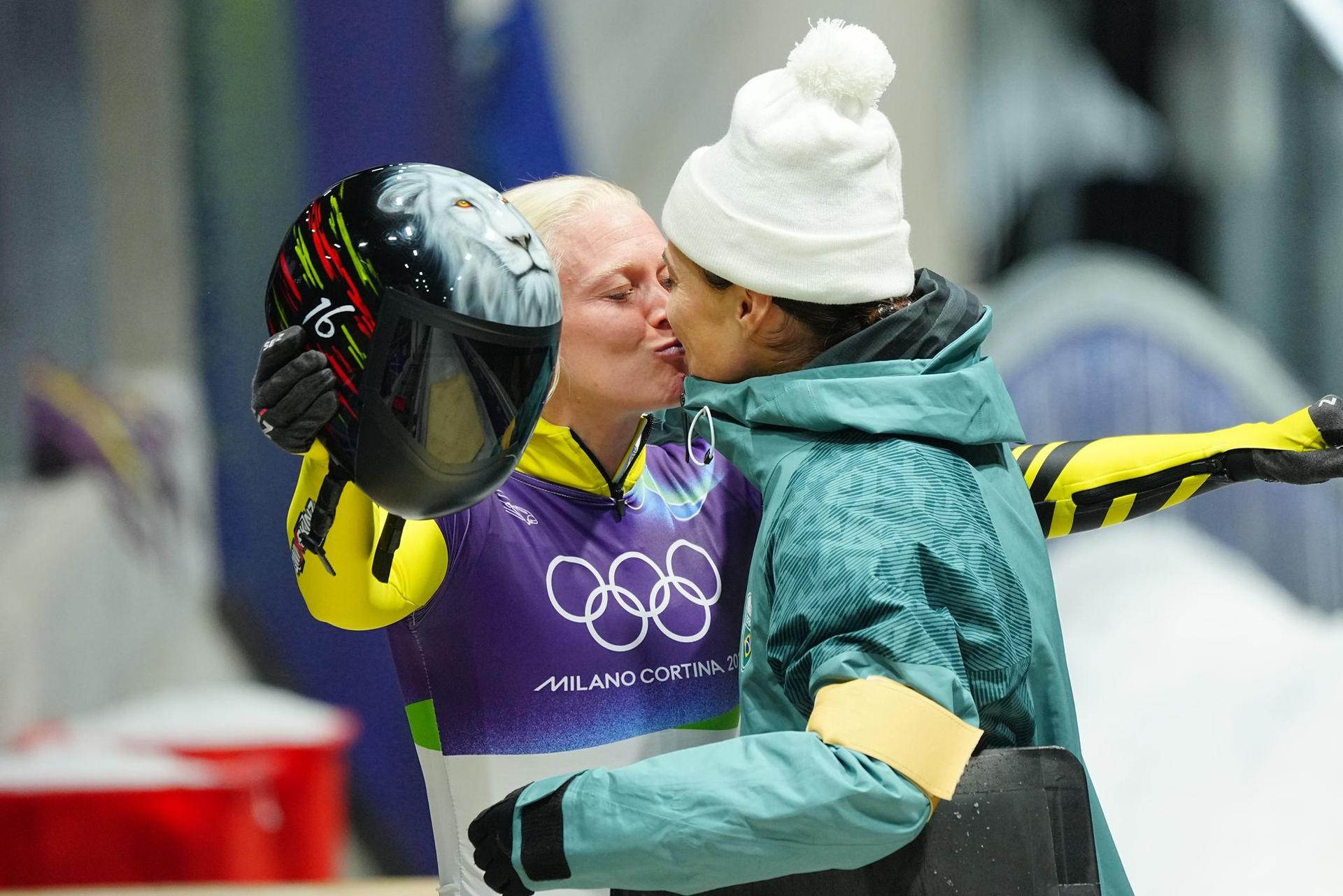 Die belgische Skeletonfahrerin Kim Meylemans (links) und ihre Frau Nicole Silveira, die für Brasilien antrat, küssen sich im Ziel. (Bild: Michael Kappeler/dpa)