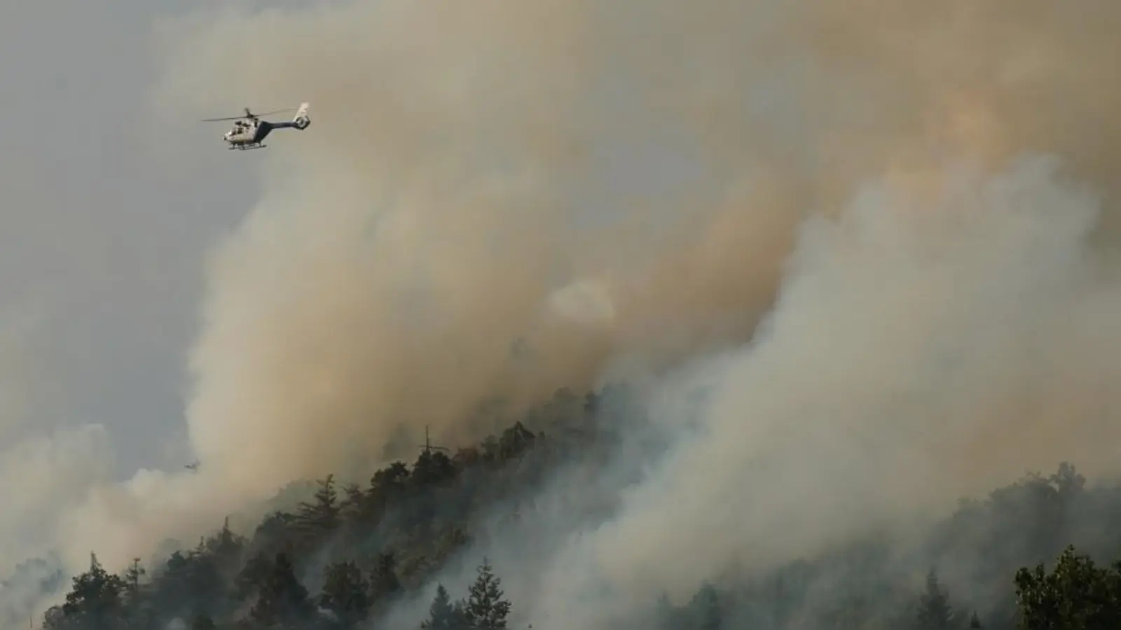 Ein Hubschrauber fliegt über den Johannisberg in Freudenberg. Dicke Rauchschwaden zeugen am Freitagabend von einem ausufernden Waldbrand. Die Menschen sind aufgerufen, Fenster und Türen geschlossen zu halten. (Bild: Rudi Wilhelm)