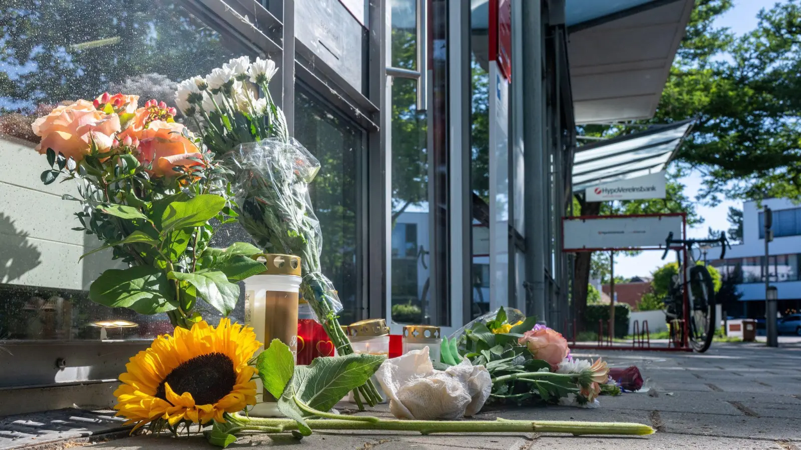 Menschen legten nach dem tödlichen Angriff Blumen und Kerzen vor der Filiale ab. (Bild: Armin Weigel/dpa)