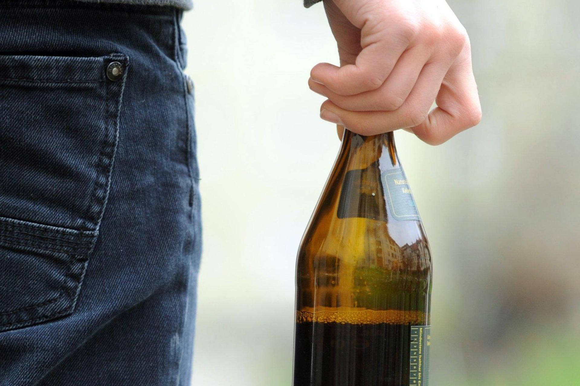 Eine Person hält eine geöffnete Bierflasche in der Hand. In Regensburg hat ein 29-Jähriger mit einer geworfenen Flasche eine Frau im Gesicht verletzt. (Symbolbild: Tobias Hase /dpa)
